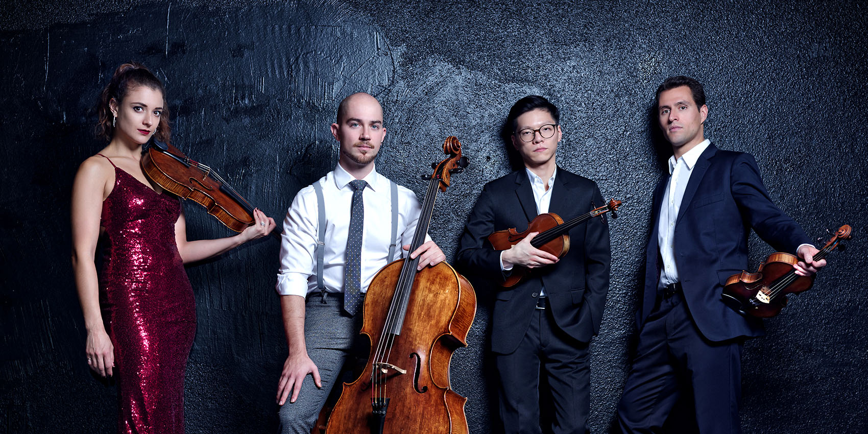 Four musicians pose with their string instruments against a dark background