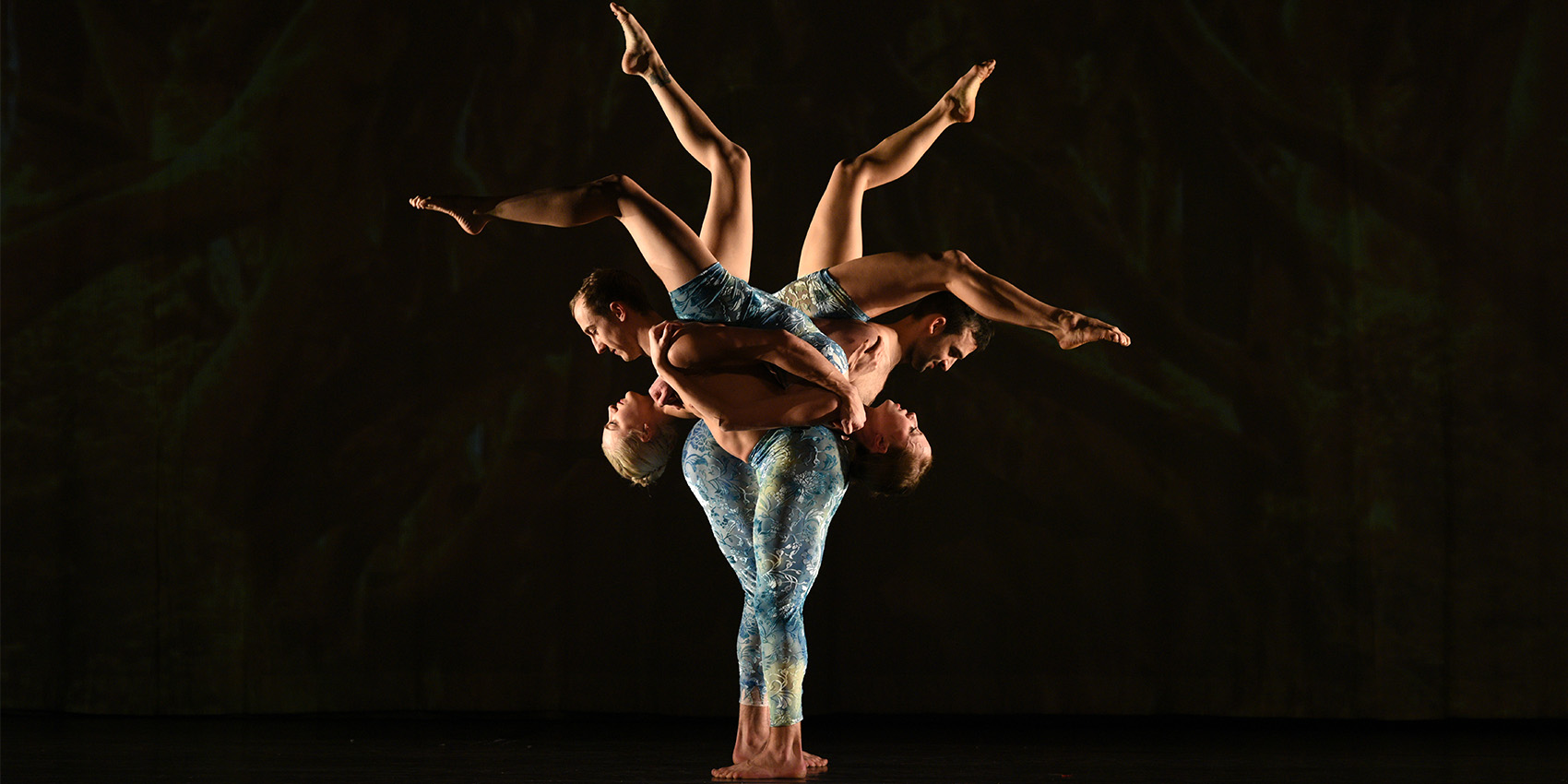Several dancers lined up in a row.  Teh dancers in the front are standing while the dancers in the back are elevated with legs in the air.