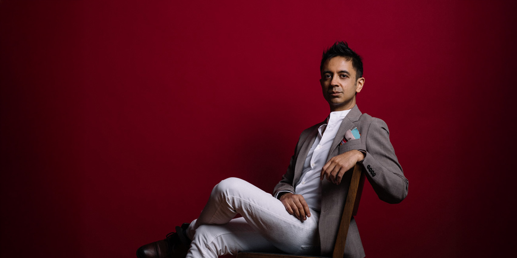 Person in suit sits in chair against red background
