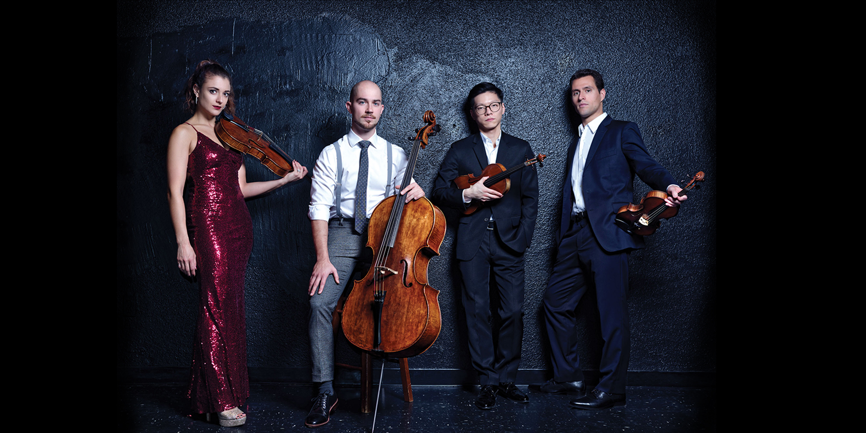 Four musicians, three male and one female, holding instruments in front of a gray background. 