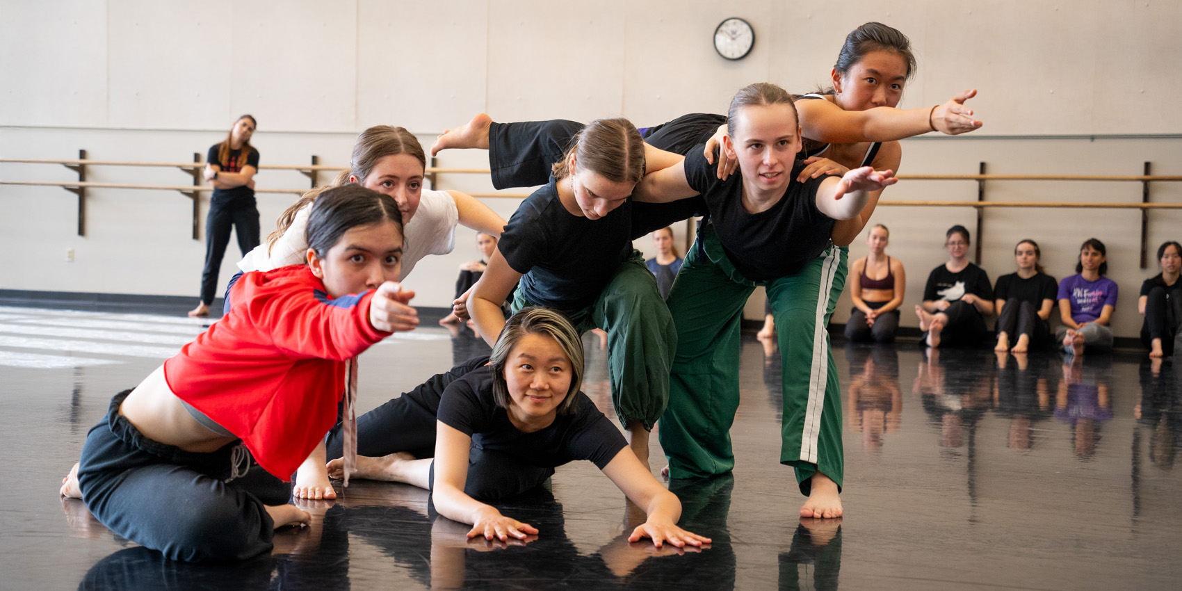 Group of dancers kneel in formation and reach toward camera