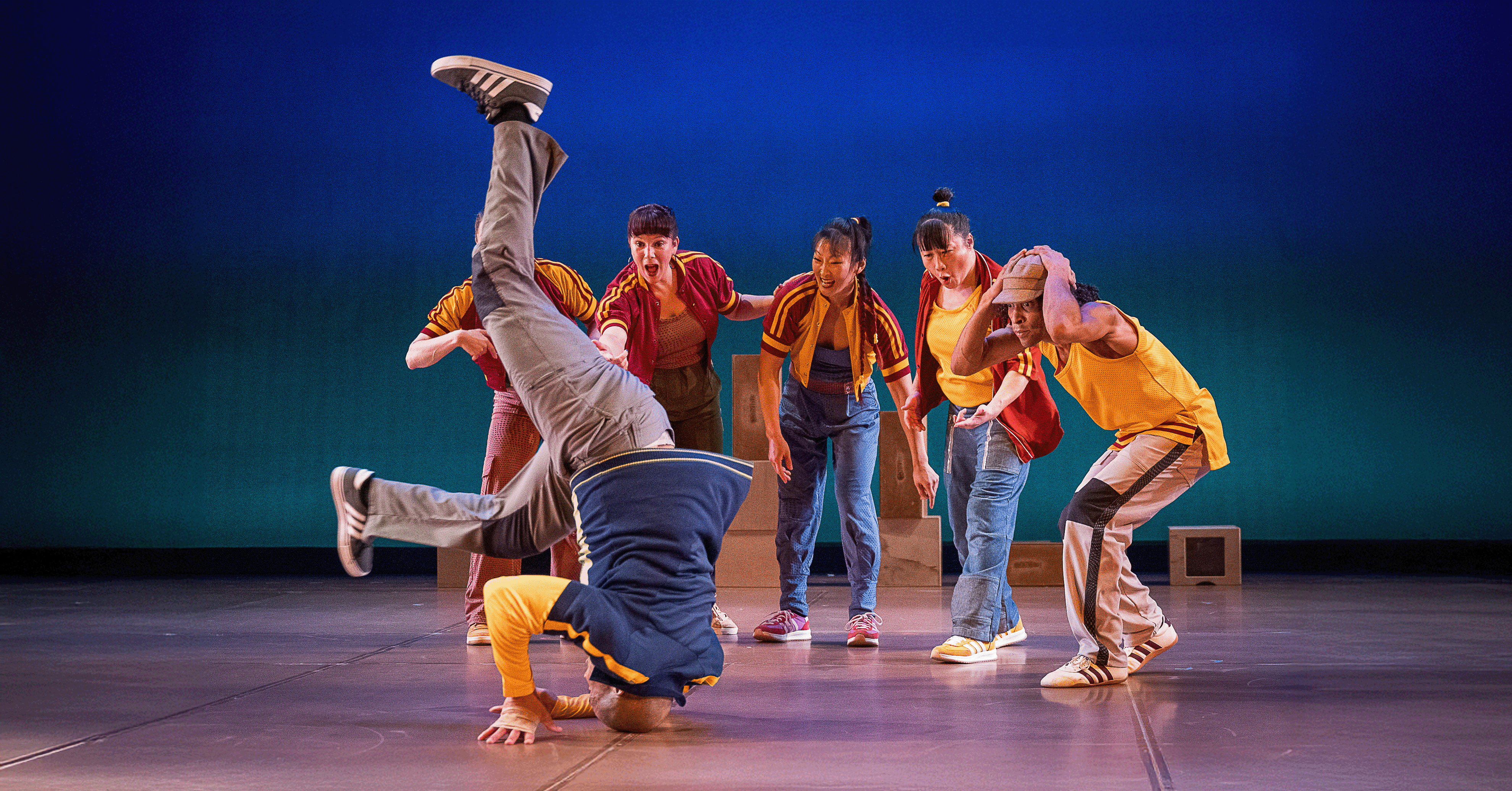 Group of dancers gape at another dancer spinning on their head