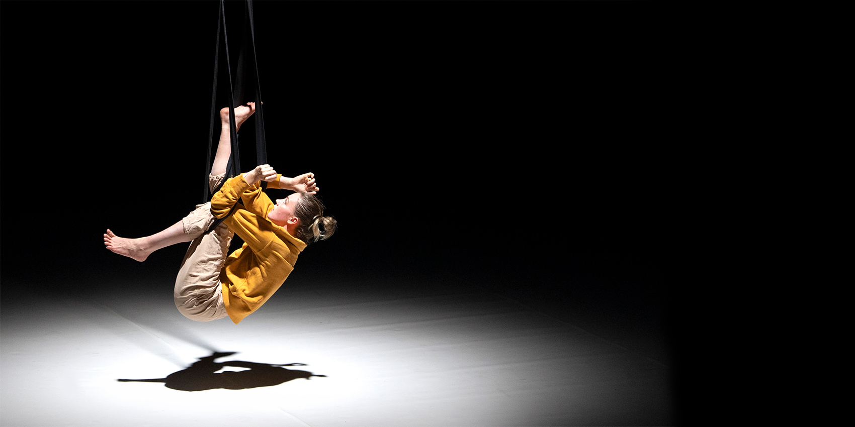 An acrobatic performer in a white spotlight on a black stage