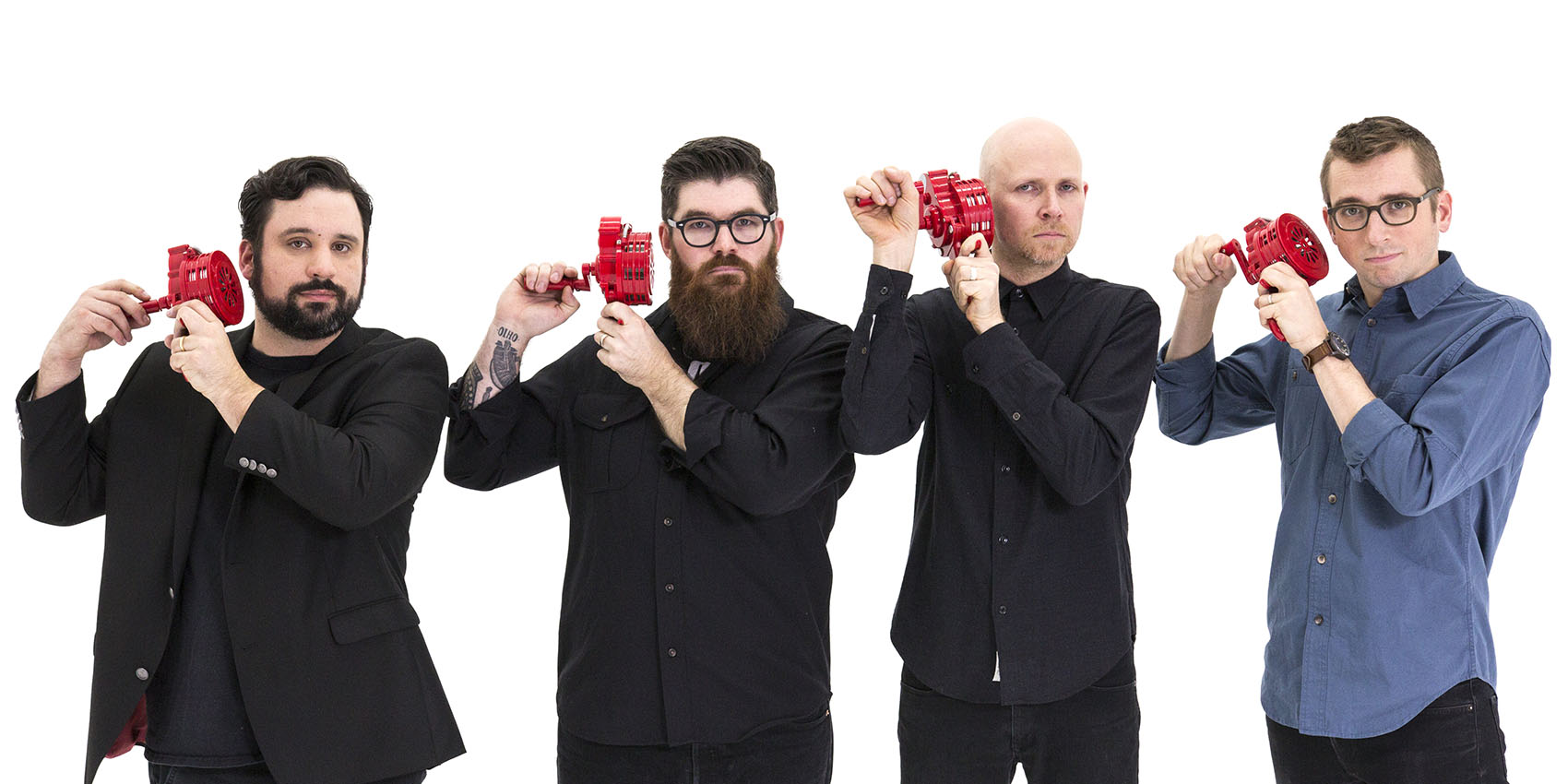 Four men holding red hand-held noisemakers in front of a white background.