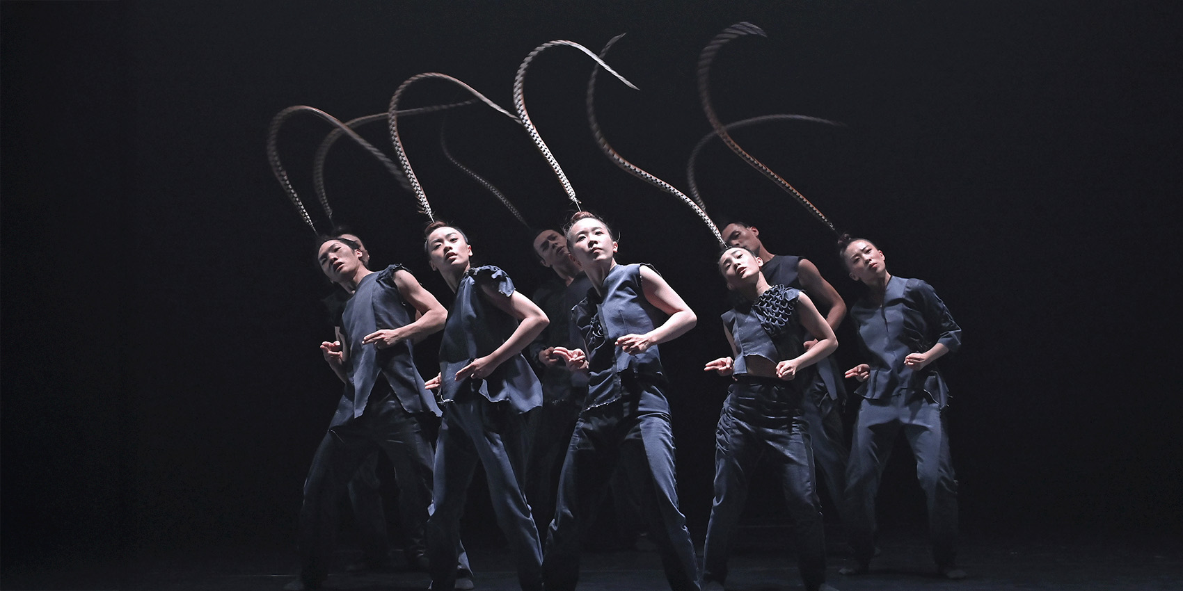 Group of dancers in black with long individual feathers on heads