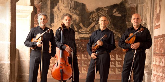 Four performers stand with their string instruments in a hallway