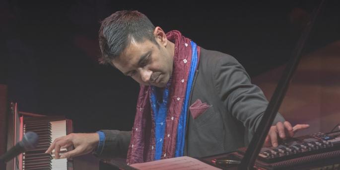 Musician in black suit with patterned scarf plays keyboard