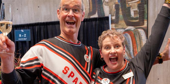 Two people in spartan cheer uniforms jump excitedly at camera
