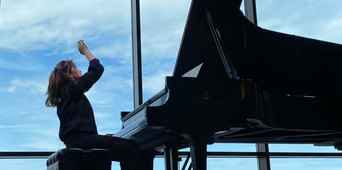 Player sits and plays at piano against blue sky background