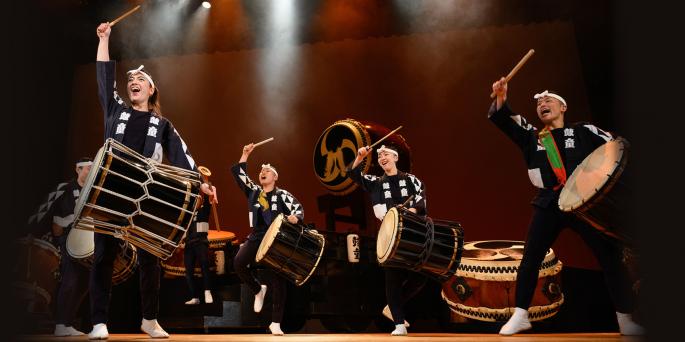 Four drummers in traditional Japanese outfits perform on stage