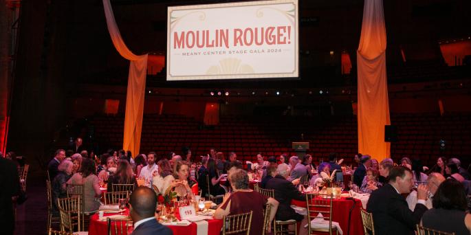 People seated at tables look at projected image that says "Moulin Rouge!"
