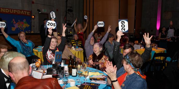 People attending a formal event sit at table and hold up auction paddles