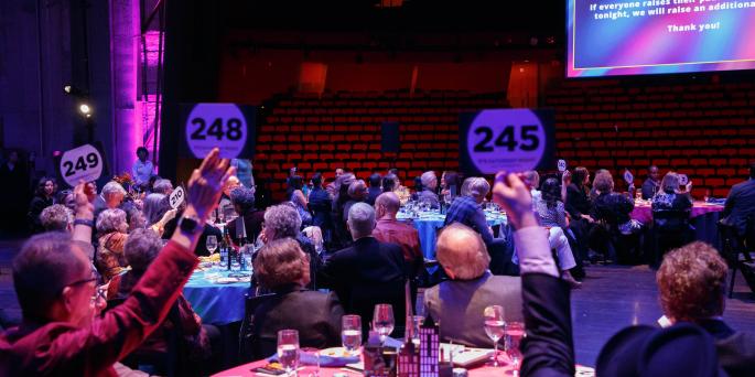 People attending a formal event sit at a table and hold up auction paddles