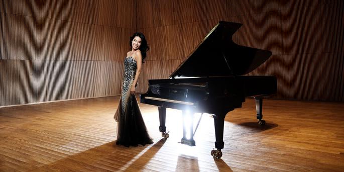 Woman in an evening dress standing next to a grand piano on stage. 