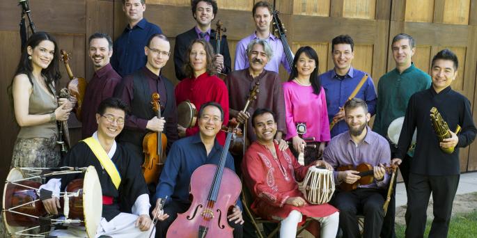 A group of musicians standing a sitting, some holding instruments.