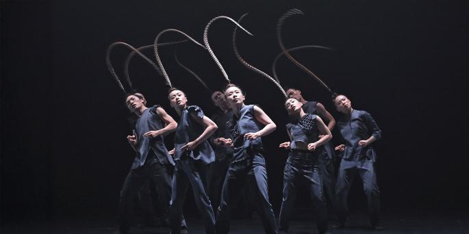 Group of dancers in black with long individual feathers on heads