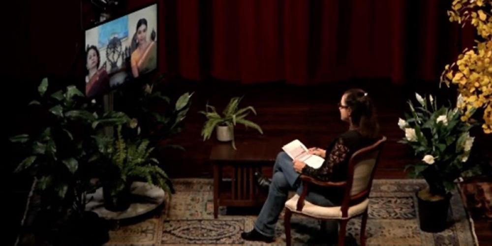 Woman sitting in a chair watching three people on a television screen. 