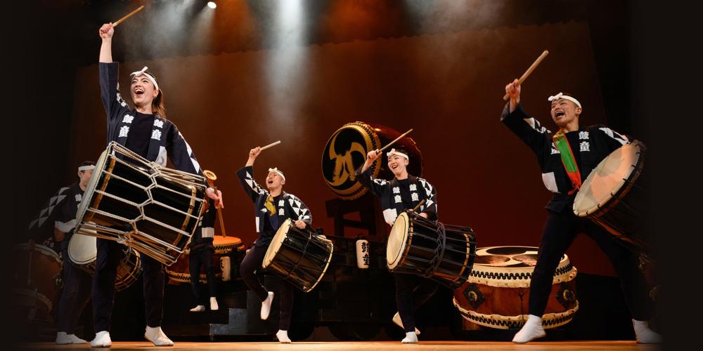 Four drummers in traditional Japanese outfits perform on stage