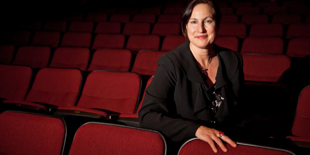 women in black blazer sits in empty theatre with red seats