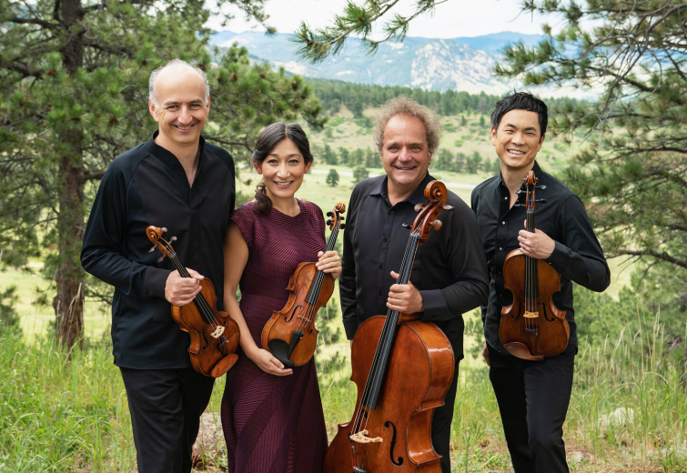 Four musicians pose with their instruments while standing outside in a natural scene