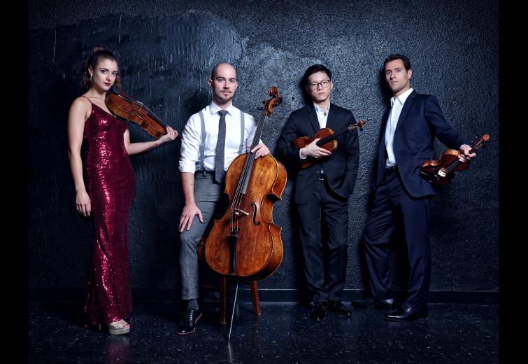 Four musicians in formal wear pose with their instruments in front of a dark background