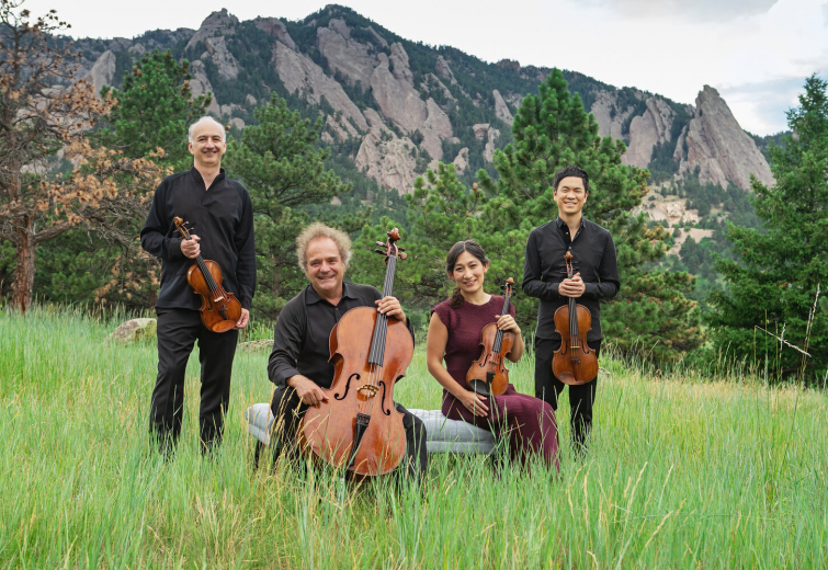 Four musicians pose with their instruments in a field in front of the Rocky Mountain Flatirons