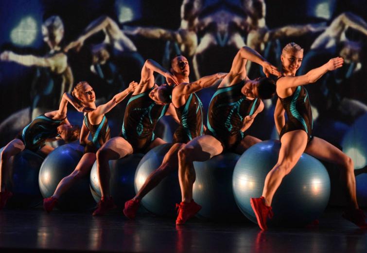 Six MOMIX performers on exercise balls against a dark background