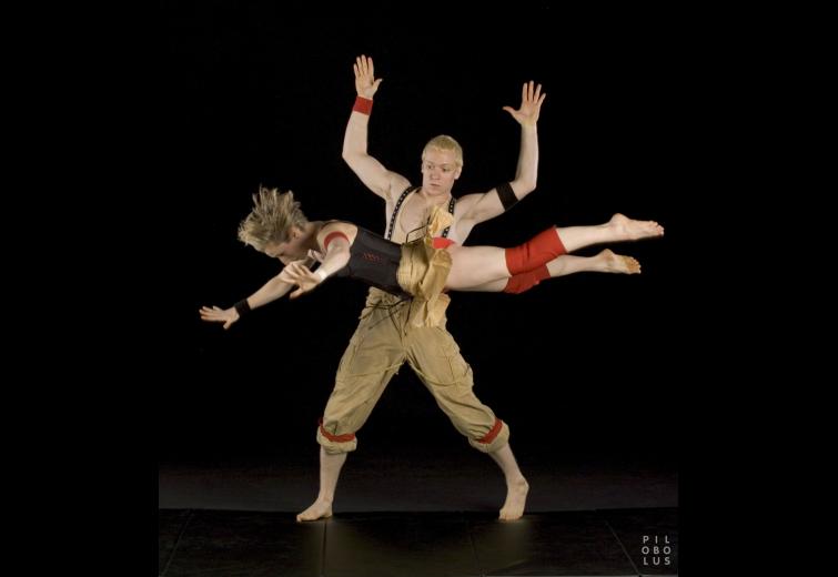 Two performers in a dynamic position against a black background