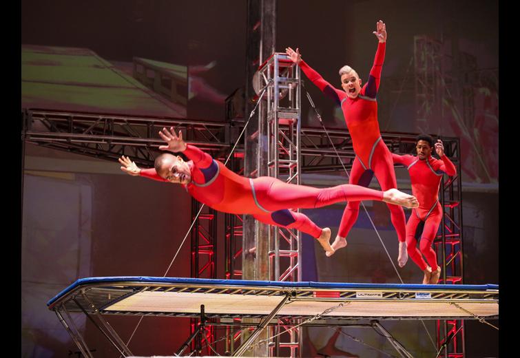 Three Streb performers in aerial poses performing on a trampoline