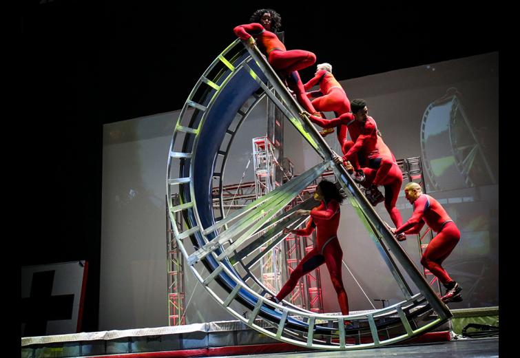 Five Streb performers in red jumpsuits performing on an acrobatic apparatus