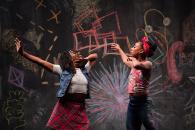 Two female dancers on stage in front of a colorful chalk wall