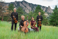 Four musicians pose with their instruments in a field in front of the Rocky Mountain Flatirons