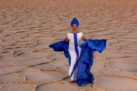 The performer stands outside in the desert with a flowing costume